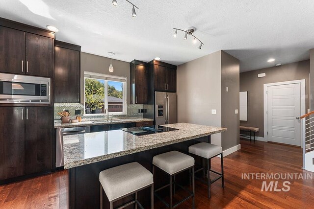 kitchen with appliances with stainless steel finishes, a kitchen bar, dark brown cabinetry, decorative backsplash, and a textured ceiling