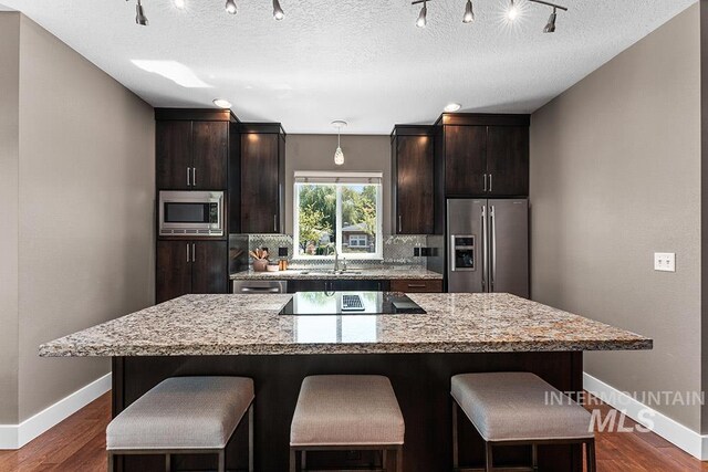 kitchen with appliances with stainless steel finishes, baseboards, a kitchen bar, a center island, and dark wood finished floors