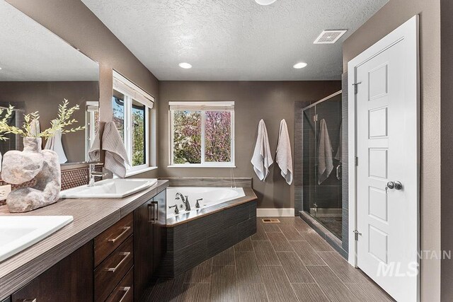 full bathroom featuring a bath, a stall shower, a textured ceiling, double vanity, and recessed lighting