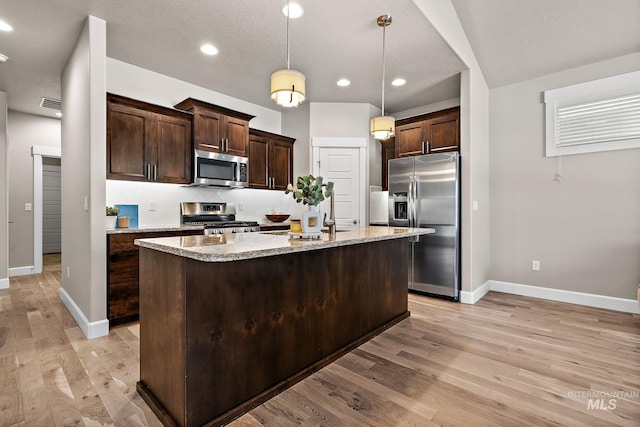1457 Summerheights, Meridian, ID 83646 - kitchen with dark brown cabinets, baseboards, an island with sink, light wood finished floors, and appliances with stainless steel finishes
