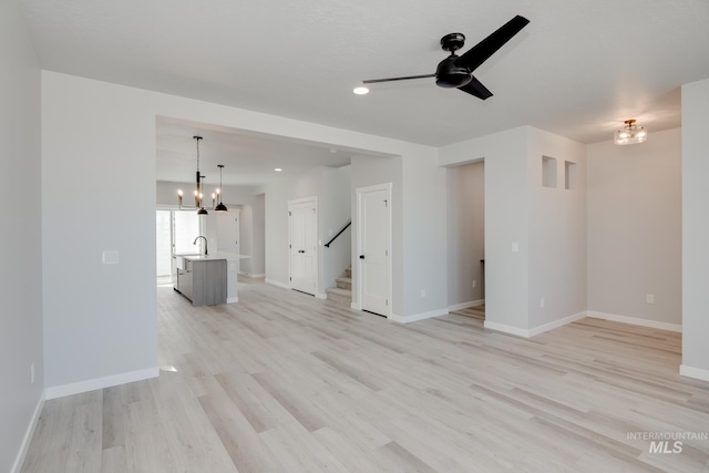 unfurnished living room featuring sink, light hardwood / wood-style floors, and ceiling fan with notable chandelier