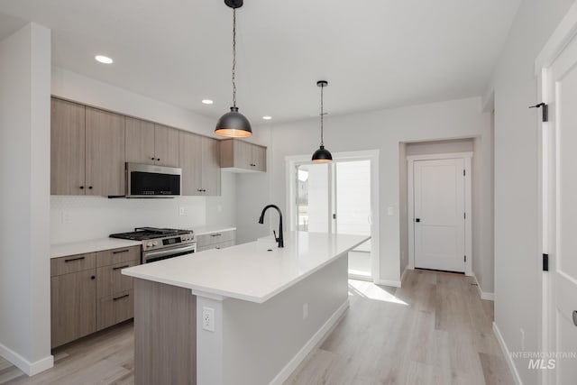 kitchen with a center island with sink, stainless steel appliances, pendant lighting, sink, and light hardwood / wood-style flooring