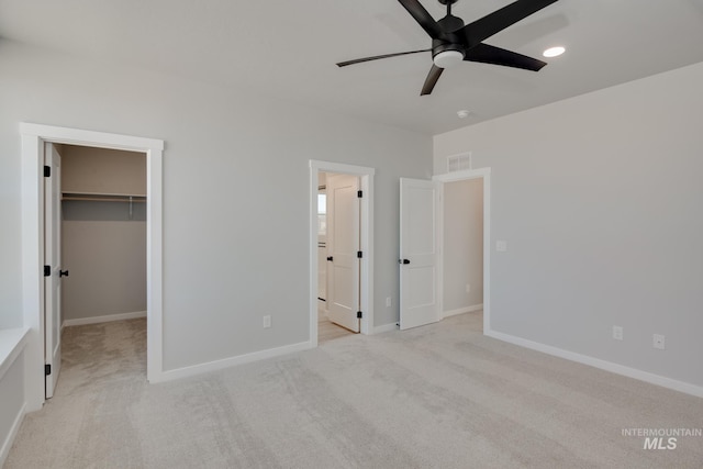 unfurnished bedroom with light colored carpet, ceiling fan, a walk in closet, and a closet