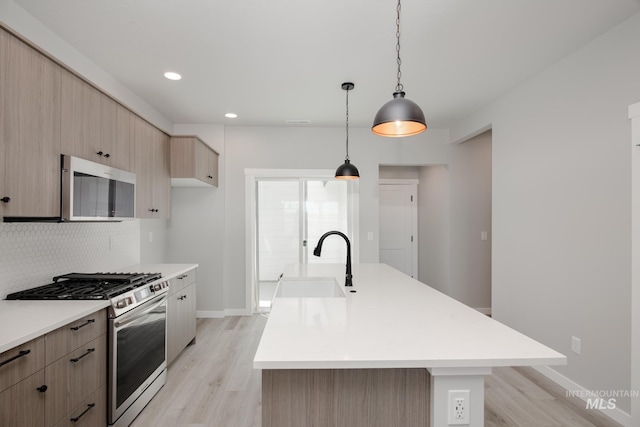 kitchen with light hardwood / wood-style flooring, appliances with stainless steel finishes, sink, and a kitchen island with sink