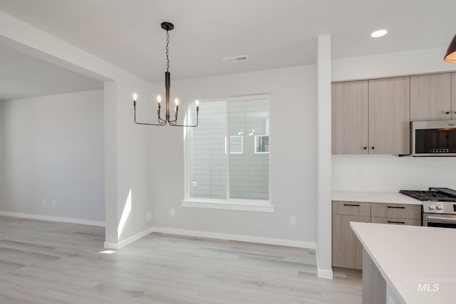 kitchen featuring appliances with stainless steel finishes, pendant lighting, light brown cabinetry, a chandelier, and light wood-type flooring