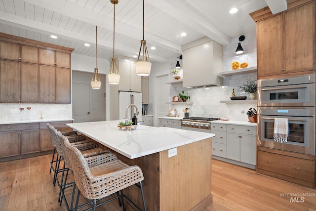 kitchen with beamed ceiling, custom range hood, backsplash, and a kitchen island with sink