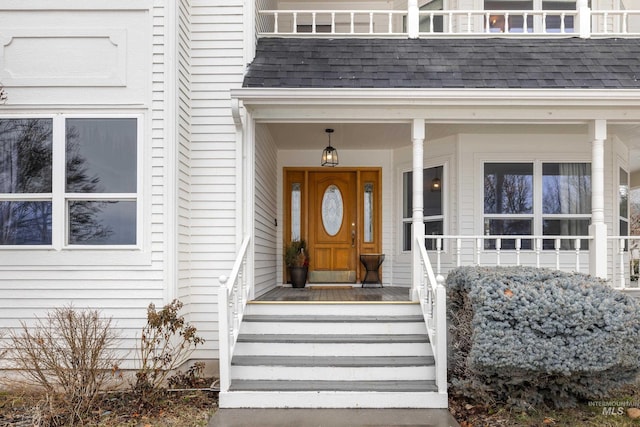 doorway to property with a shingled roof and a porch