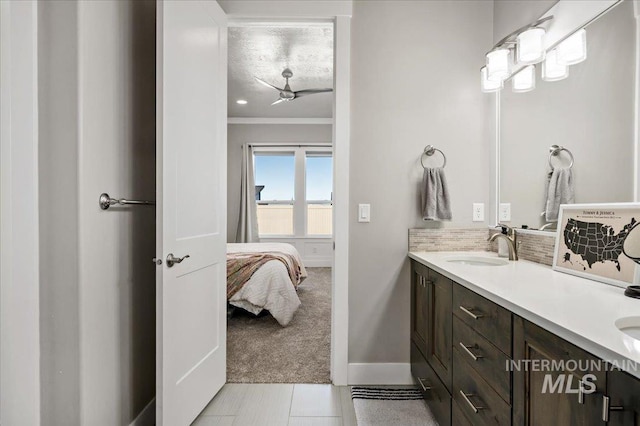 ensuite bathroom with double vanity, backsplash, ornamental molding, a sink, and baseboards