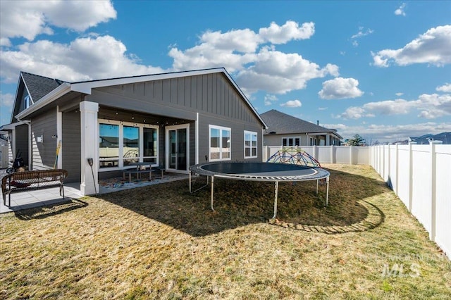 rear view of property featuring a fenced backyard, a trampoline, a yard, a patio area, and board and batten siding