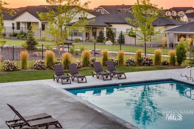 pool at dusk featuring a residential view, a patio, a community pool, and fence