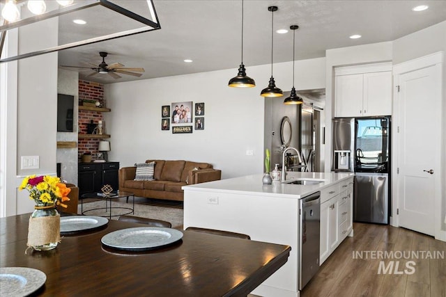 kitchen featuring white cabinets, open floor plan, wood finished floors, a sink, and stainless steel dishwasher