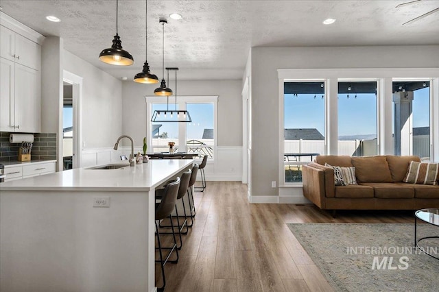 kitchen featuring light countertops, hanging light fixtures, light wood-style flooring, white cabinetry, and a sink