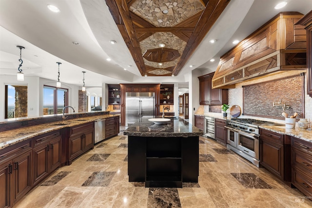 kitchen featuring high end appliances, sink, a large island with sink, decorative light fixtures, and dark stone countertops