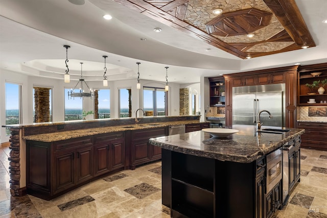 kitchen featuring appliances with stainless steel finishes, a wealth of natural light, a raised ceiling, a large island with sink, and hanging light fixtures