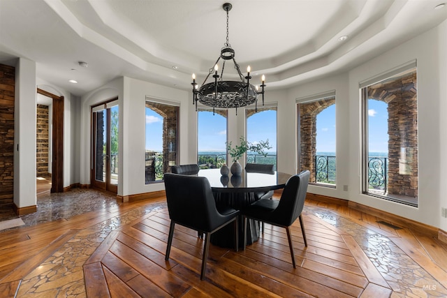 dining area with a raised ceiling, dark wood-type flooring, a healthy amount of sunlight, and an inviting chandelier