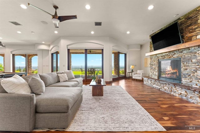 living room with hardwood / wood-style floors, plenty of natural light, ceiling fan, and a stone fireplace