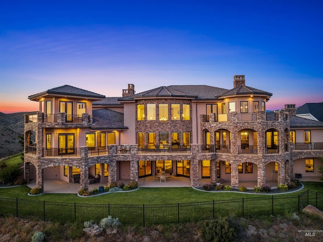 back house at dusk with a lawn, a patio area, and a balcony