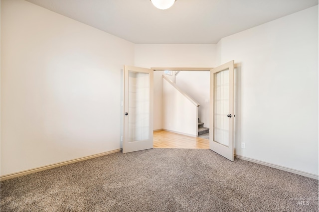 carpeted empty room featuring french doors, baseboards, and stairs