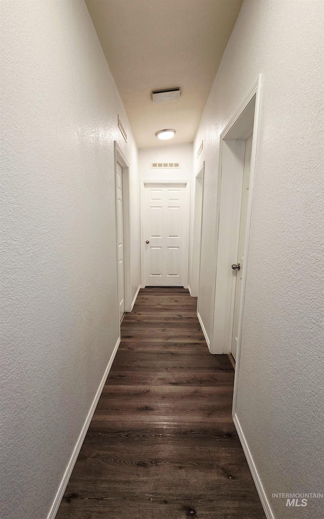 hall with dark wood-style flooring, visible vents, a textured wall, and baseboards