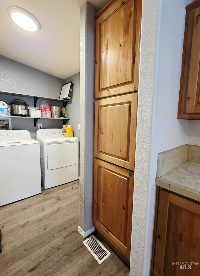 washroom featuring visible vents, a textured wall, light wood-style flooring, and separate washer and dryer