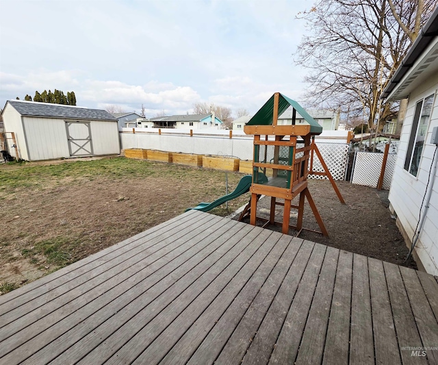 wooden deck featuring a playground, an outdoor structure, a fenced backyard, and a storage unit