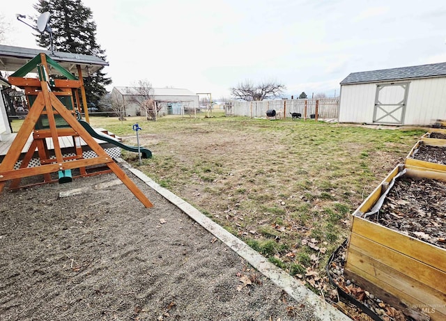 view of yard with a playground, an outdoor structure, fence, a vegetable garden, and a storage unit