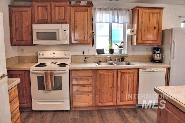 kitchen with dark wood-style floors, white appliances, a sink, and brown cabinets