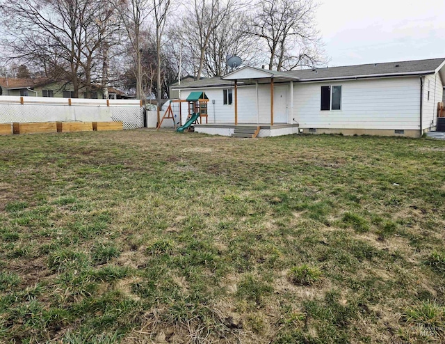 rear view of house with a playground, a lawn, entry steps, crawl space, and fence