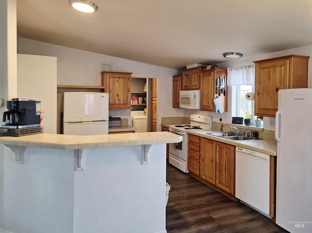 kitchen with a breakfast bar area, tile counters, a sink, washer / dryer, and white appliances