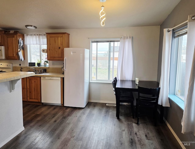 kitchen with brown cabinets, tile countertops, dark wood-type flooring, white appliances, and baseboards