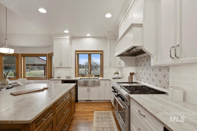 kitchen with sink, stainless steel stove, light stone counters, pendant lighting, and white cabinets