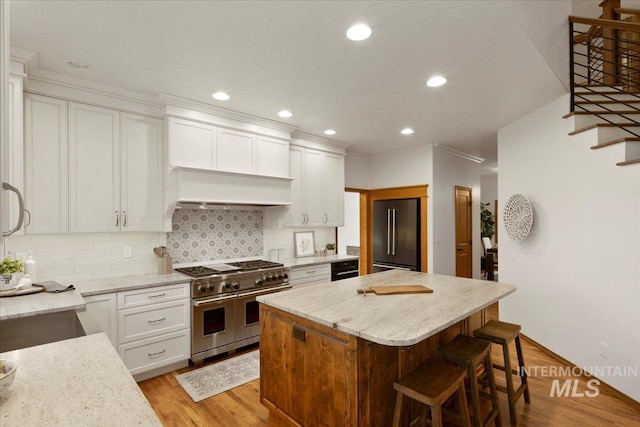 kitchen with high quality appliances, a center island, white cabinets, and light hardwood / wood-style flooring