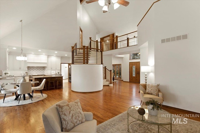 living room with ceiling fan, high vaulted ceiling, and light hardwood / wood-style flooring