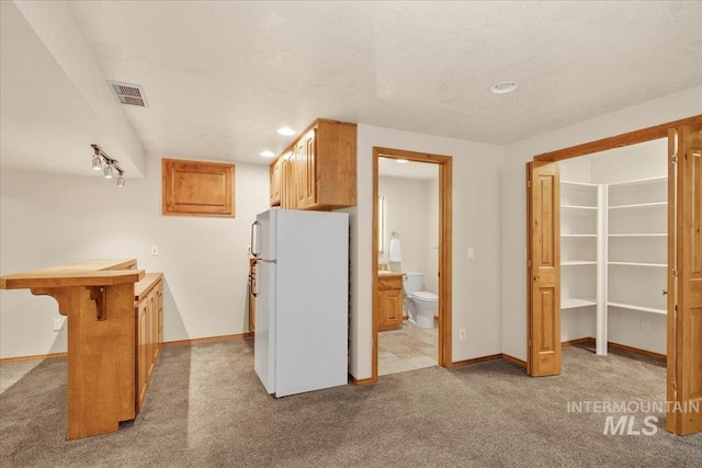 kitchen featuring a breakfast bar, a textured ceiling, white refrigerator, and light colored carpet