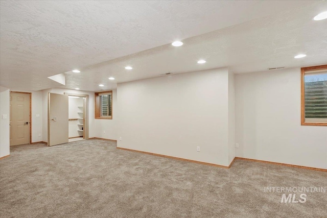 basement featuring light colored carpet and a textured ceiling