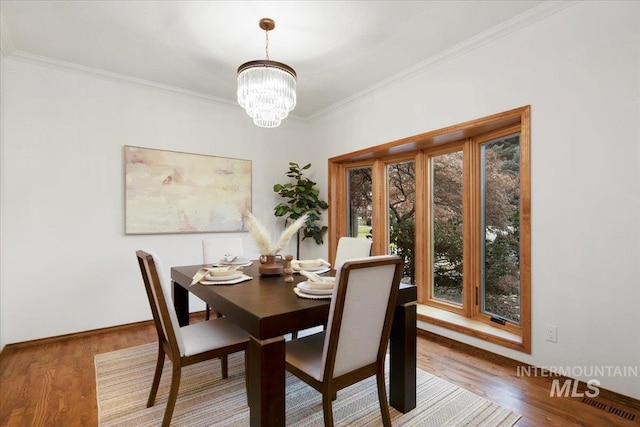 dining area with hardwood / wood-style floors, ornamental molding, and an inviting chandelier