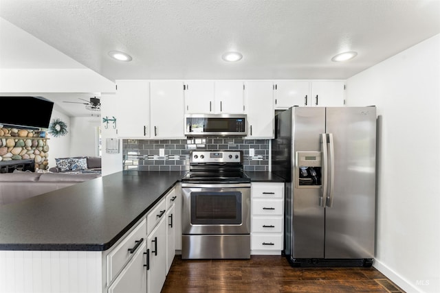 kitchen featuring dark countertops, appliances with stainless steel finishes, a ceiling fan, a peninsula, and dark wood-style floors