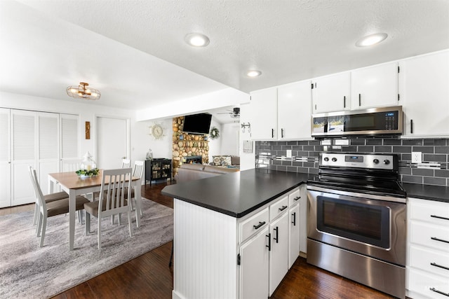 kitchen with a peninsula, dark countertops, dark wood-type flooring, tasteful backsplash, and stainless steel appliances