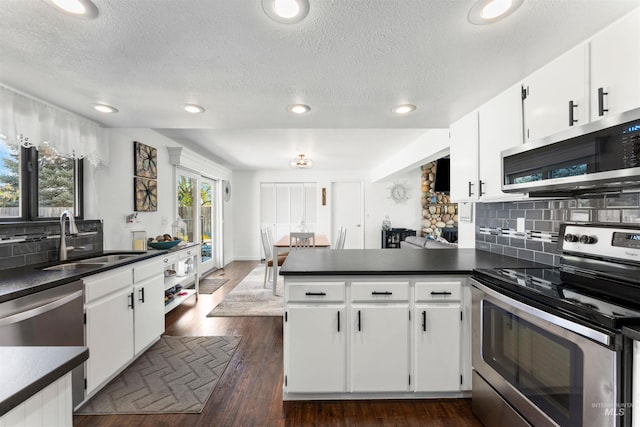 kitchen featuring a sink, stainless steel appliances, white cabinetry, a peninsula, and backsplash