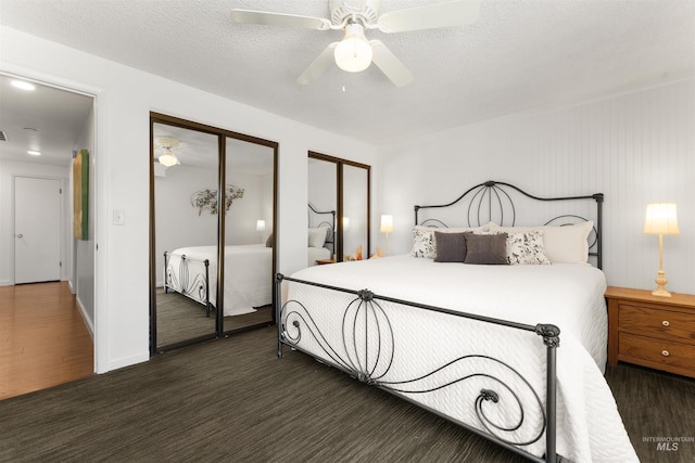 bedroom with two closets, dark wood-style flooring, a ceiling fan, and baseboards