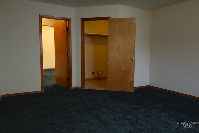 unfurnished bedroom featuring dark colored carpet, a spacious closet, and a closet