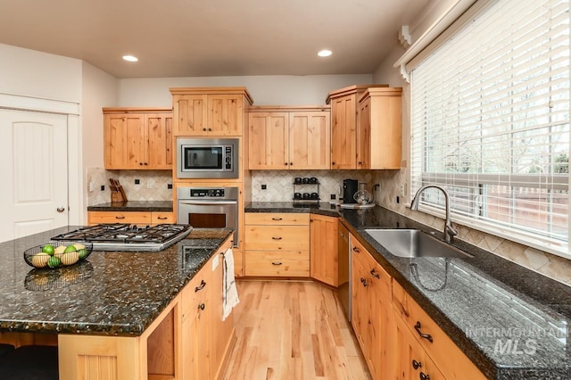 kitchen with sink, stainless steel appliances, dark stone countertops, light hardwood / wood-style floors, and decorative backsplash