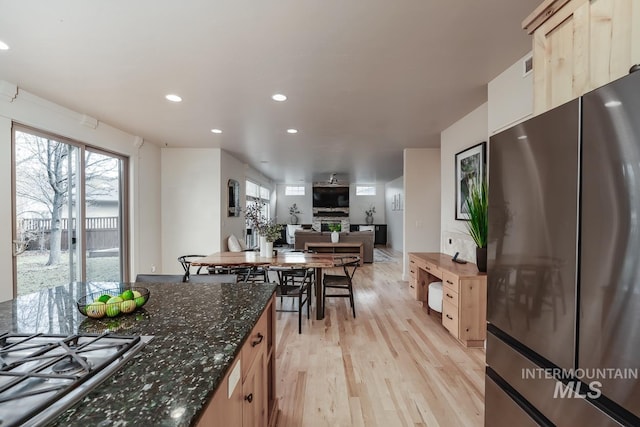 kitchen with cooktop, light brown cabinets, light hardwood / wood-style floors, a stone fireplace, and fridge