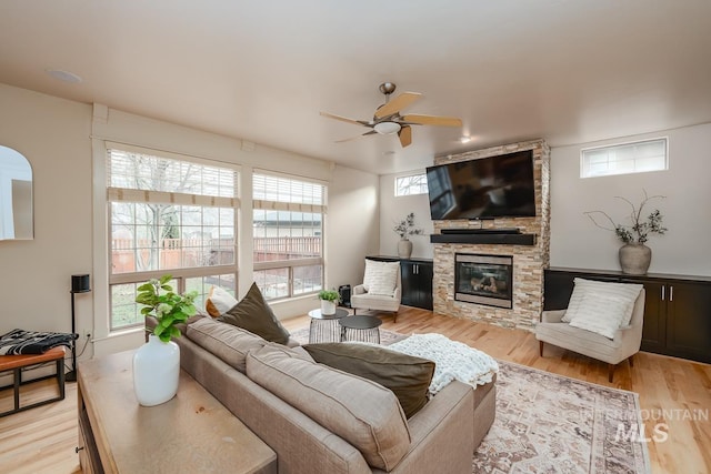 living room with ceiling fan, a stone fireplace, and light wood-type flooring