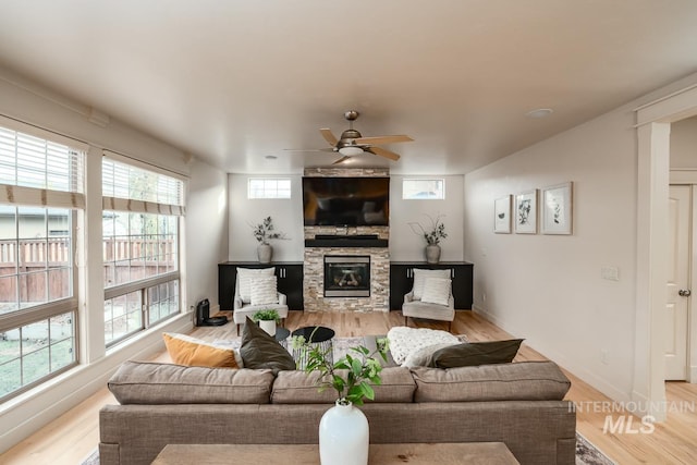 living room with light hardwood / wood-style floors, a stone fireplace, ceiling fan, and plenty of natural light