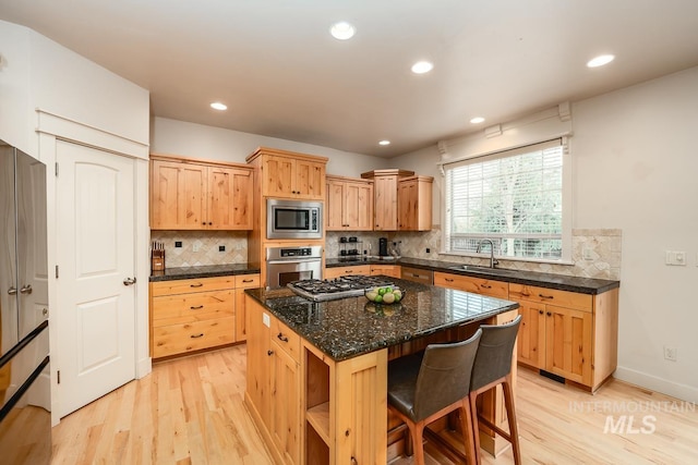 kitchen with sink, dark stone countertops, light wood-type flooring, appliances with stainless steel finishes, and a kitchen island