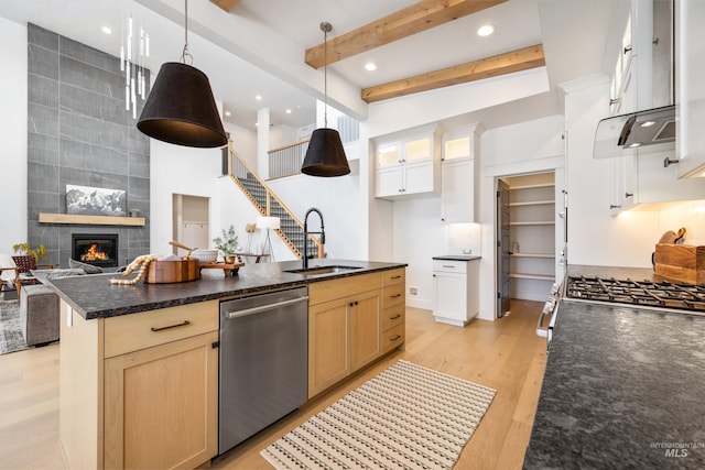 kitchen with light wood-style flooring, a sink, glass insert cabinets, dishwasher, and a tile fireplace