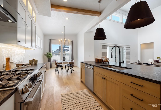 kitchen with light wood finished floors, backsplash, beamed ceiling, appliances with stainless steel finishes, and a sink