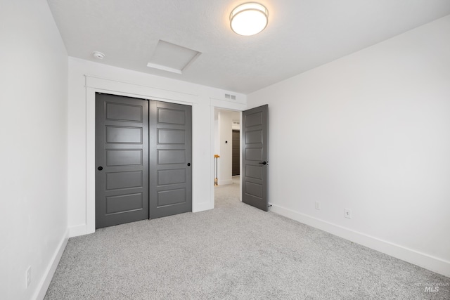 unfurnished bedroom featuring visible vents, baseboards, attic access, carpet flooring, and a closet