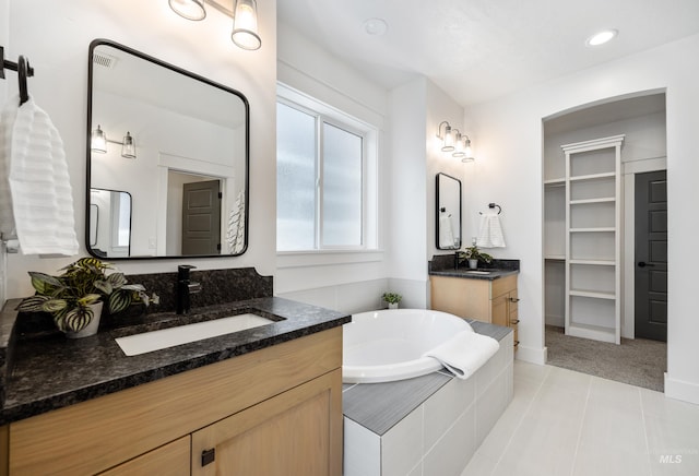 full bath featuring tile patterned flooring, a spacious closet, a garden tub, two vanities, and a sink